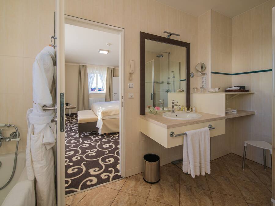 Un baño de hotel con bañera, un espejo grande, un lavabo y una ducha.