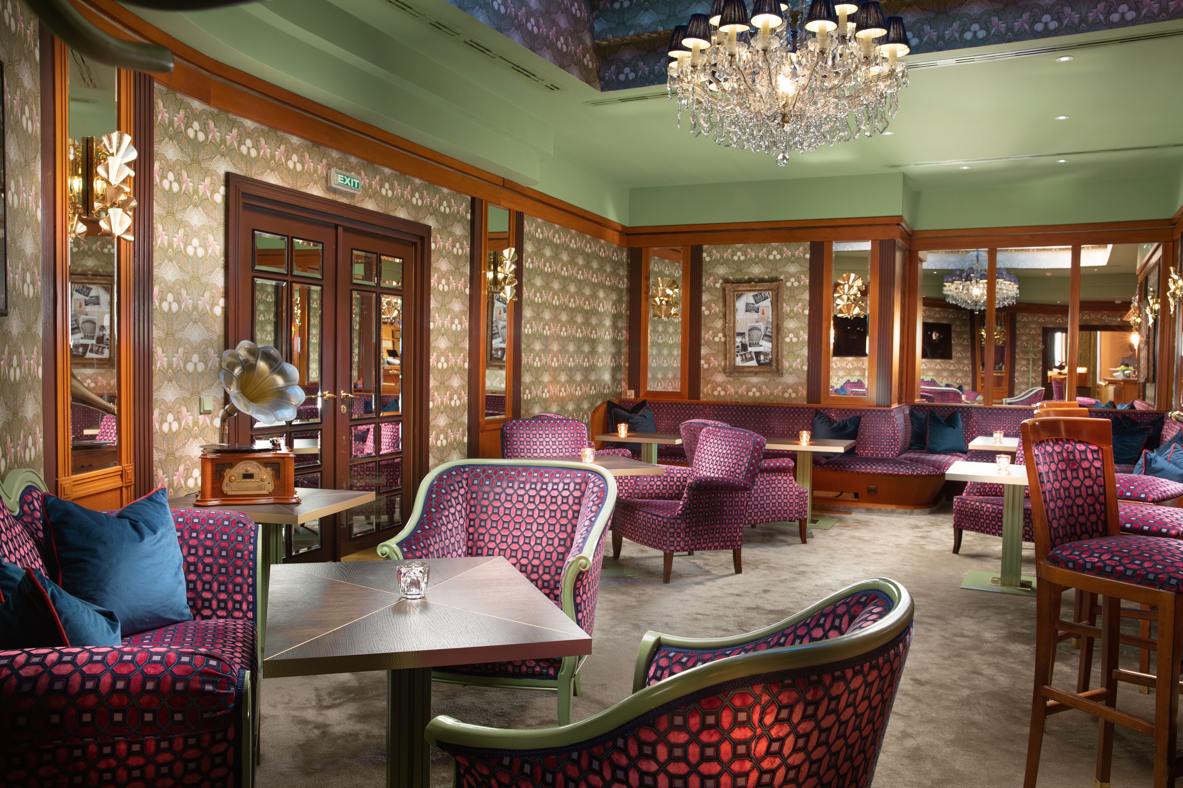 A restaurant with patterned upholstery, wooden furniture, and a chandelier.