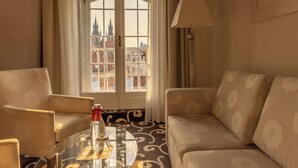 A hotel room with a sofa, armchair, and a glass table with a bottle and glasses. - Grand Hotel Bohemia (Prague)