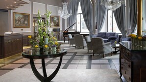 A spacious living room with a grand piano, patterned chairs, and a round glass table with floral arrangements. - Grand Hotel Bohemia (Prague)