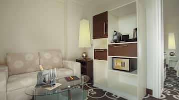 Una habitación de hotel moderna con una mesa de centro de vidrio, un sofá color beige, un armario de madera y una alfombra estampada.