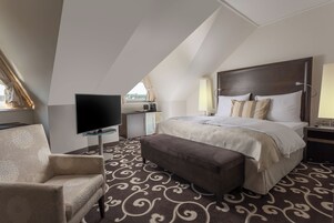 Quarto de hotel com uma cama grande, televisão de tela plana, sofá e escrivaninha com luminária.