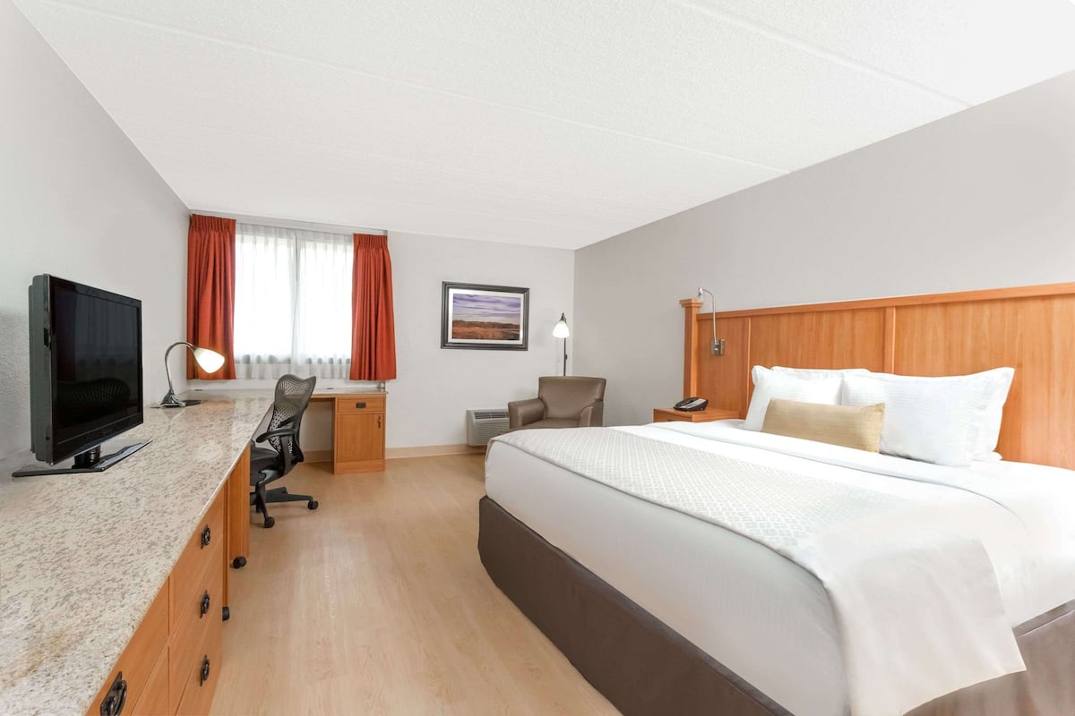 A hotel room with a bed, desk, chair, television, and a painting on the wall.
