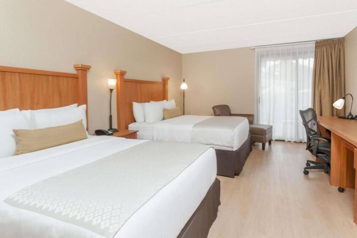 A hotel room with two beds, a desk, a chair, a lamp, and a window with curtains.