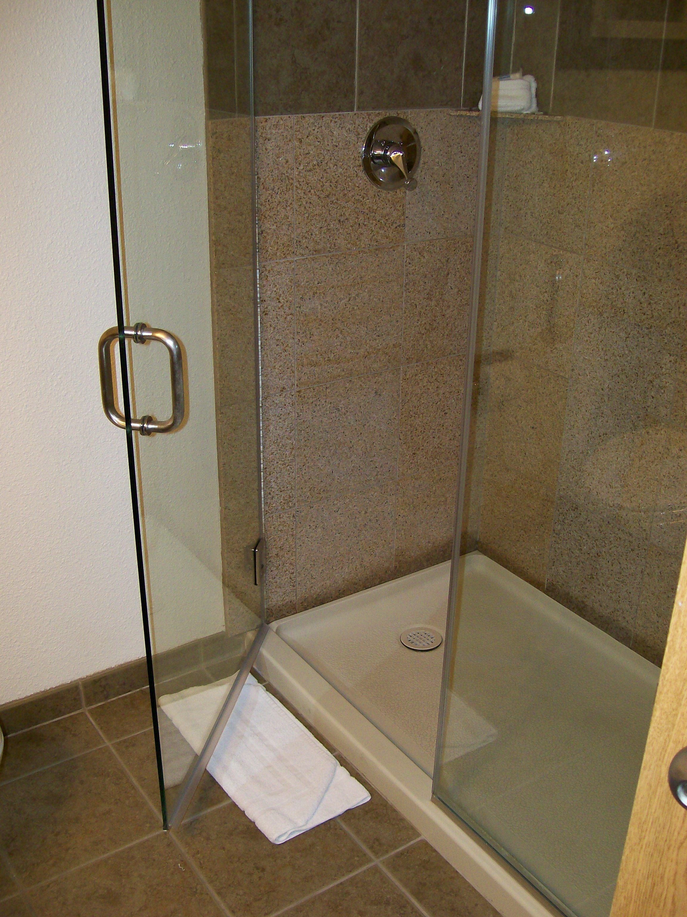 A glass-enclosed shower with a handheld showerhead, a glass door with a handle, and a white towel on the floor.