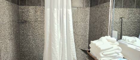 A bathroom with a bathtub, a shower curtain, a stack of white towels, and a toiletry box on a granite countertop.