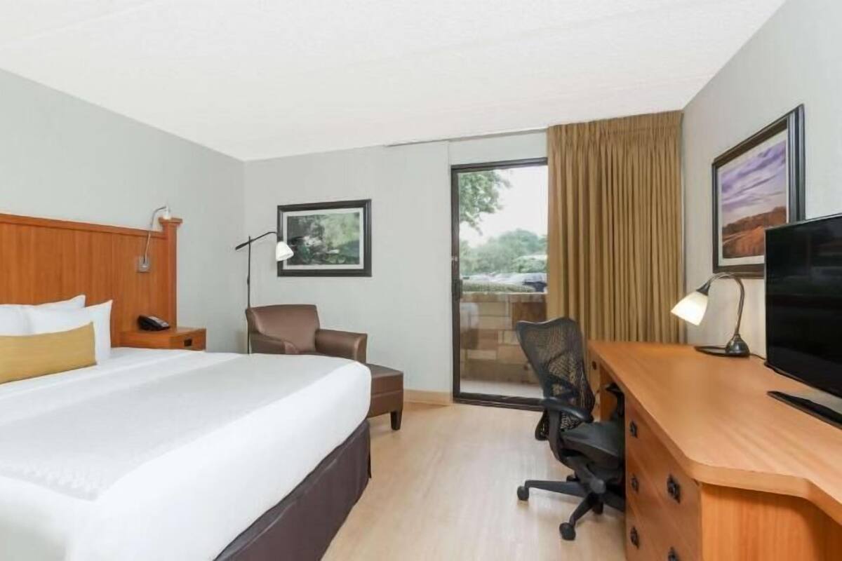 A hotel room with a bed, desk, chair, TV, and a view through a glass door.