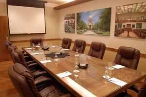 A conference room with a long table, brown leather chairs, and a projector screen.