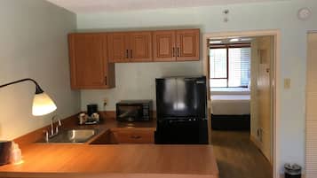 Una cocina compacta con armarios de madera, un refrigerador negro, un microondas y un lavamanos.