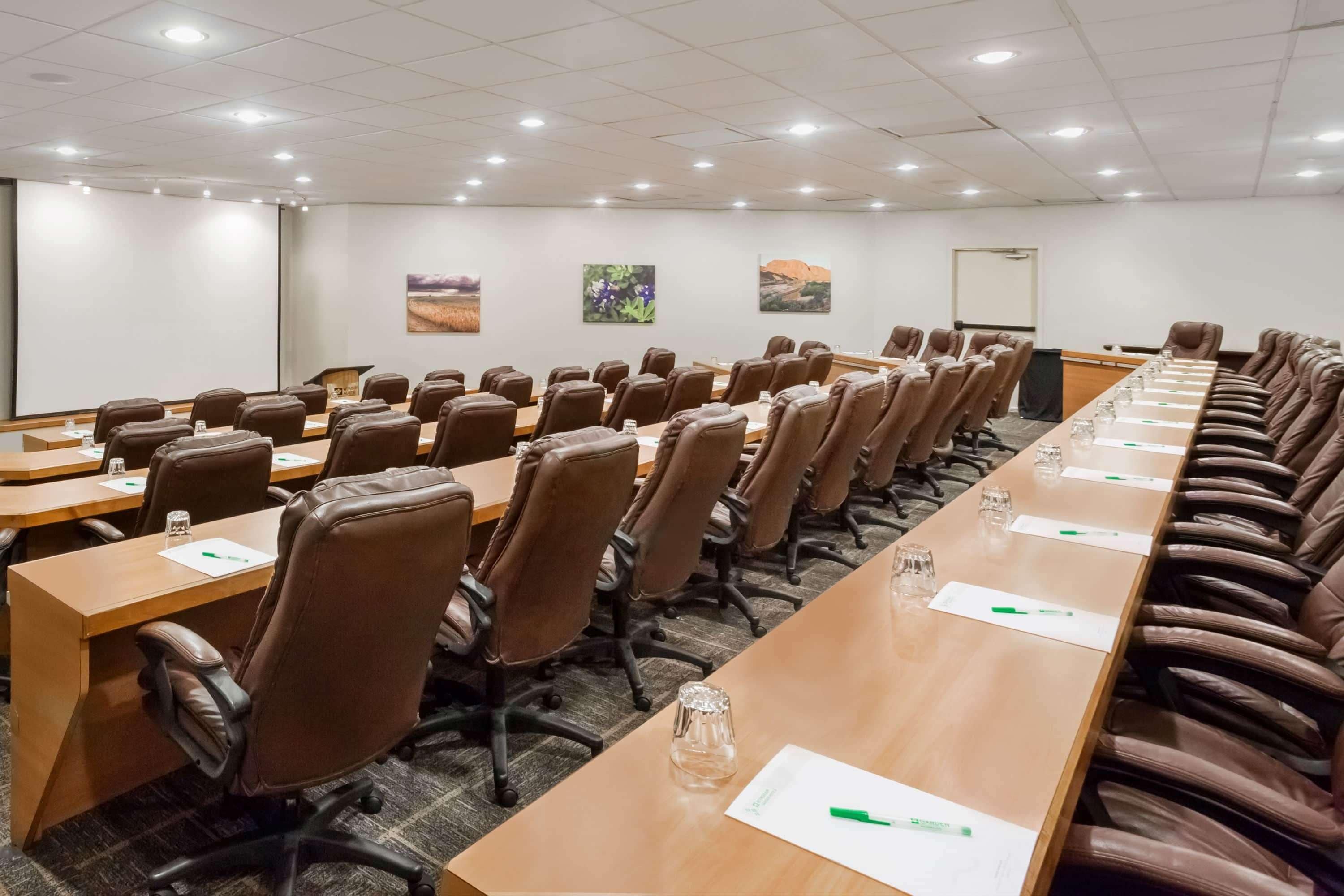 A conference room with long tables, brown leather chairs, and white walls.