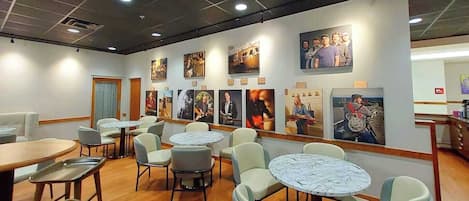 Un restaurante con mesas y sillas redondas, suelo de madera y cuadros en las paredes.
