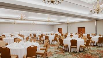 A banquet hall with round tables, chairs, chandeliers, and a carpeted floor.