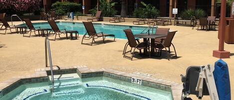 A pool area with lounge chairs and a hot tub, surrounded by palm trees and a building with a green roof.