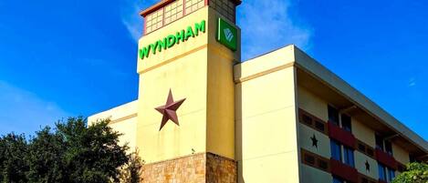 Un hotel con un llamativo letrero de 'WYNDHAM', un emblema de estrella y un cielo azul despejado al fondo.