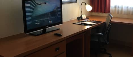 Un escritorio de madera con un monitor de computadora, una lámpara y una silla.