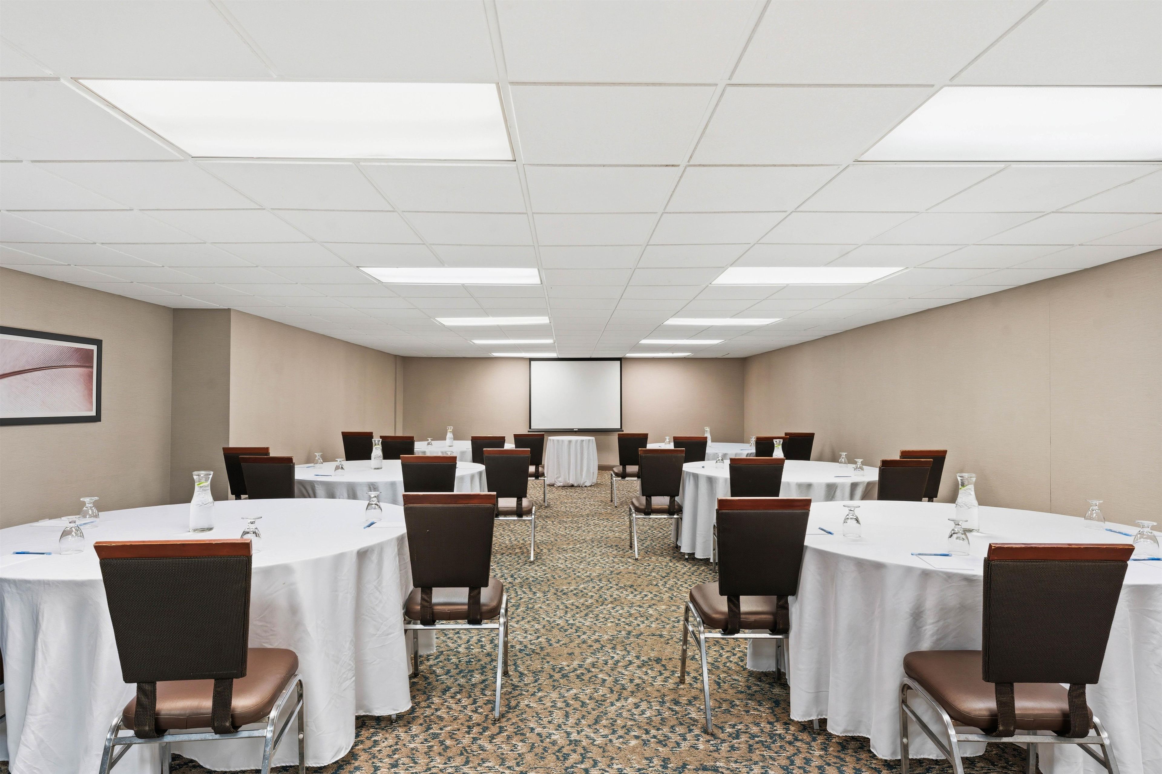 Un salón de conferencias con varias mesas redondas, sillas y una pantalla para proyector.