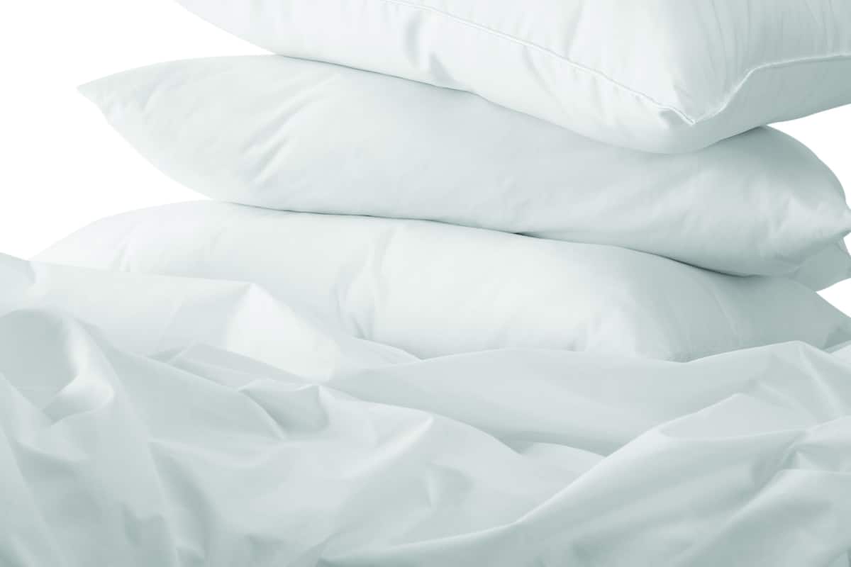 Une pile d’oreillers blancs sur un lit recouvert d’un drap blanc.