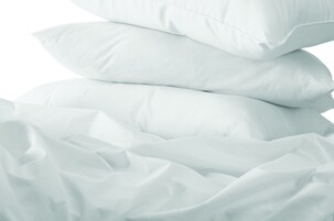 Una pila de almohadas blancas sobre una sábana blanca en una cama.