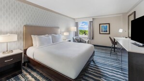 A hotel room with a large bed, a desk, a chair, a television, and a window with a view of greenery. - DoubleTree by Hilton Hotel Wilmington (Wilmington)