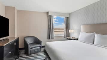A hotel room with a bed, a chair, a TV, a window with curtains, and a nightstand with a lamp.