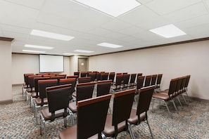 A conference room with rows of chairs, a projector screen, and a carpeted floor. - DoubleTree by Hilton Hotel Wilmington (Wilmington)