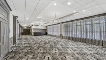 A hotel corridor with a patterned carpet, a long reception desk, and a row of windows with sheer curtains.
