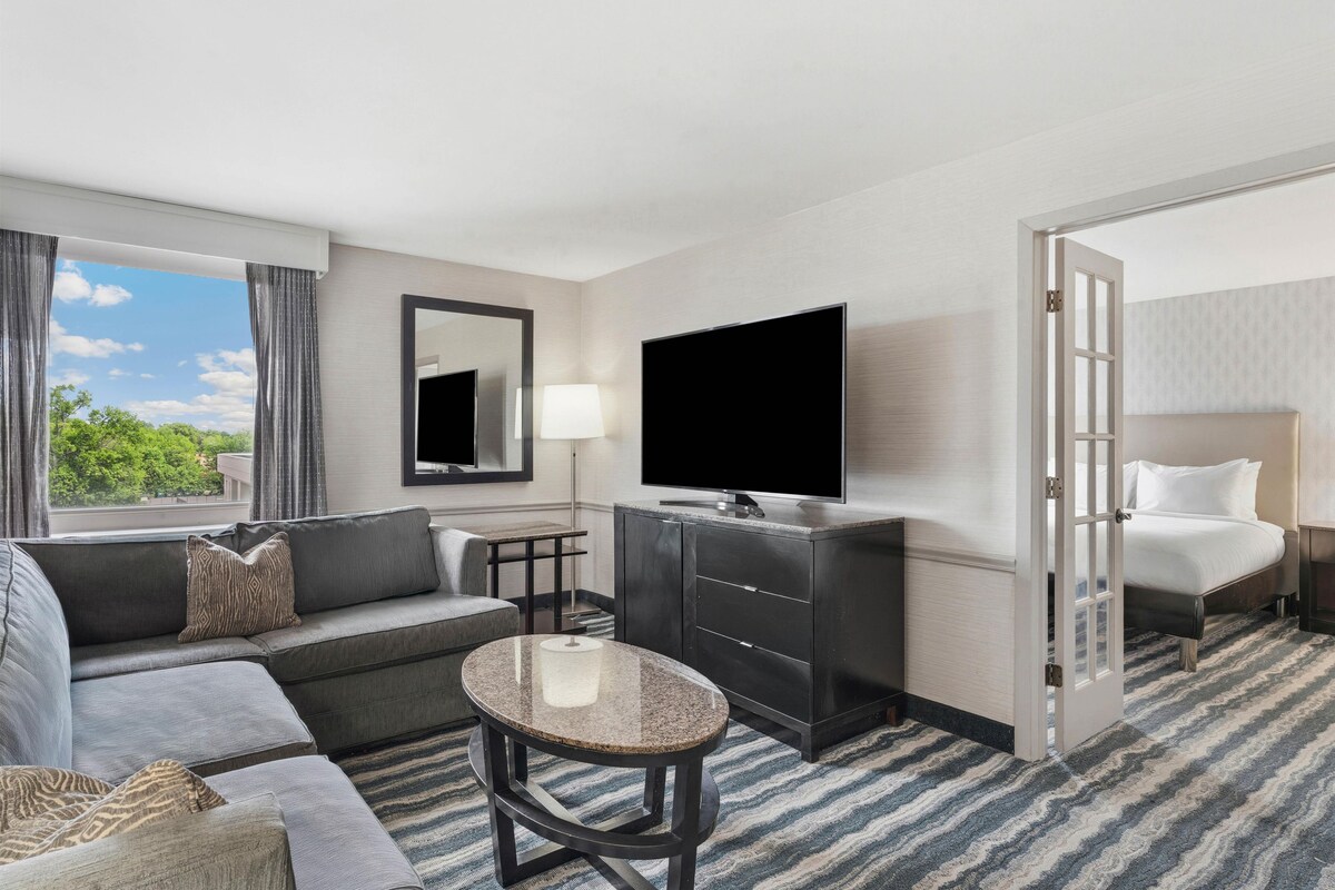 A hotel room with a sofa, a small round table, a TV, a mirror, a lamp, and a bed.