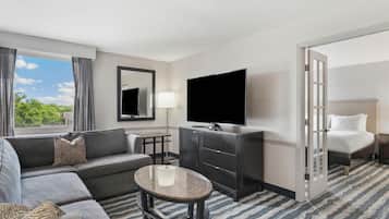 A hotel room with a sofa, a small round table, a TV, a mirror, a lamp, and a bed.