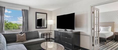 A hotel room with a sofa, a small round table, a TV, a mirror, a lamp, and a bed.