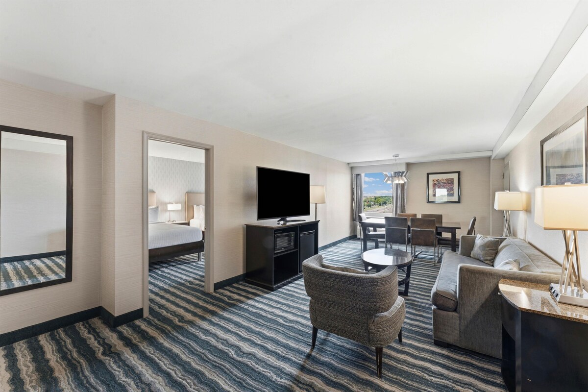 A hotel room with a bed, a television, a desk, a sofa, and a dining area with chairs.