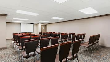Un salón de conferencias con filas de sillas, una pantalla de proyector y piso alfombrado.