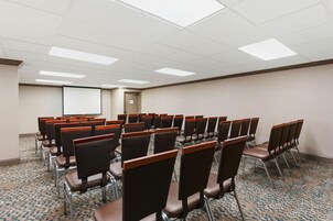 A conference room with rows of chairs, a projector screen, and a carpeted floor.