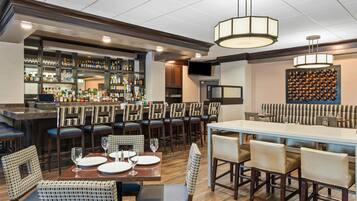 A bar area with multiple seating options, including bar stools and tables, and a variety of liquor bottles on shelves.