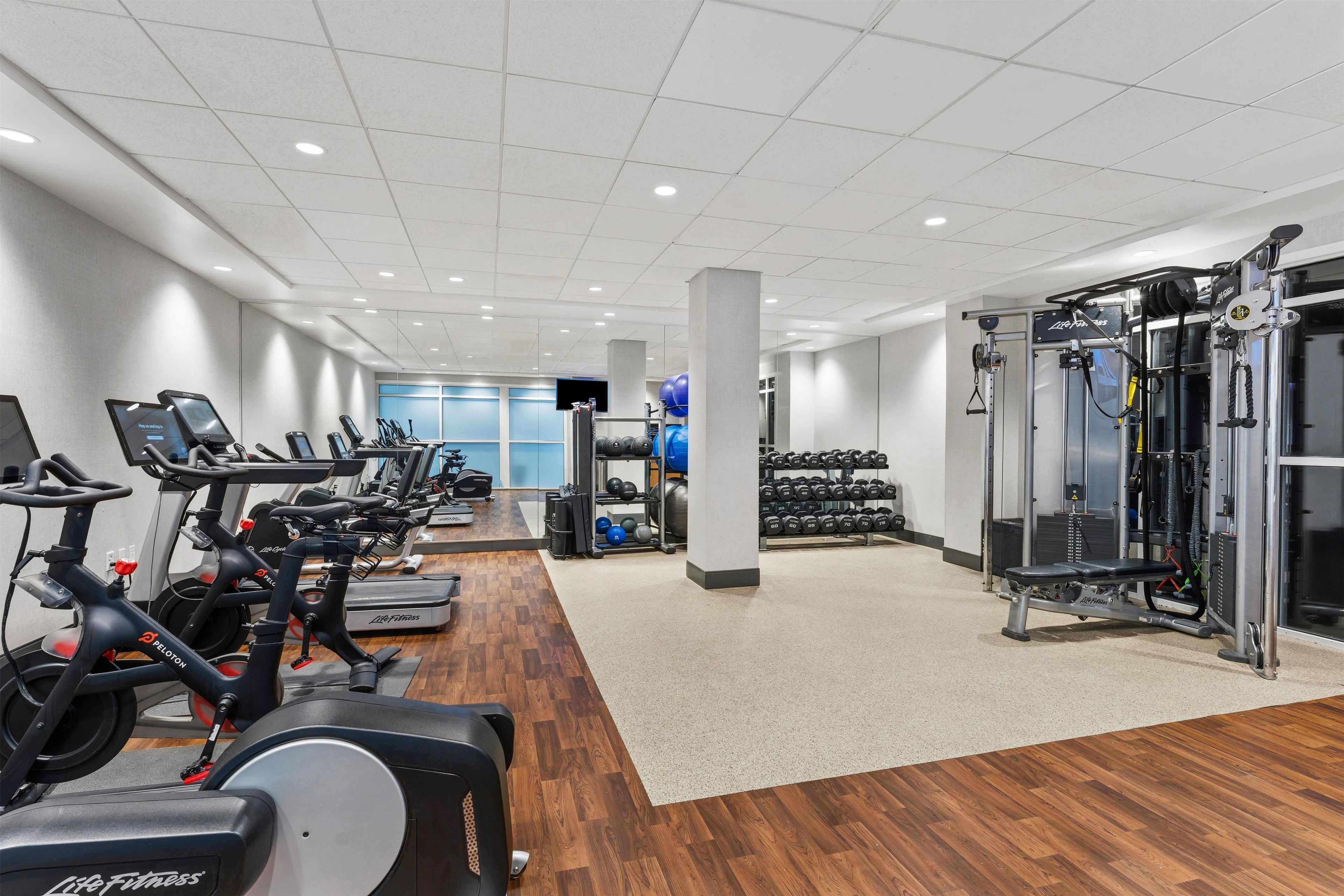 A gym with cardio machines, weightlifting equipment, and a wall-mounted TV.