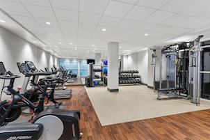 A gym with cardio machines, weightlifting equipment, and a wall-mounted TV.