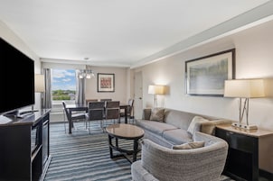 A hotel room with a dining area, a sofa, a TV, and a view of the outdoors.