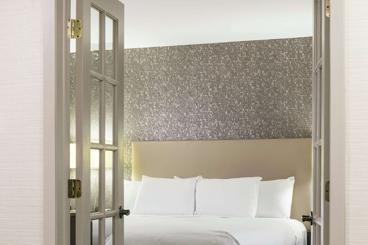 Une chambre d’hôtel avec un lit, une porte, une moquette à motifs et un mur à texture.