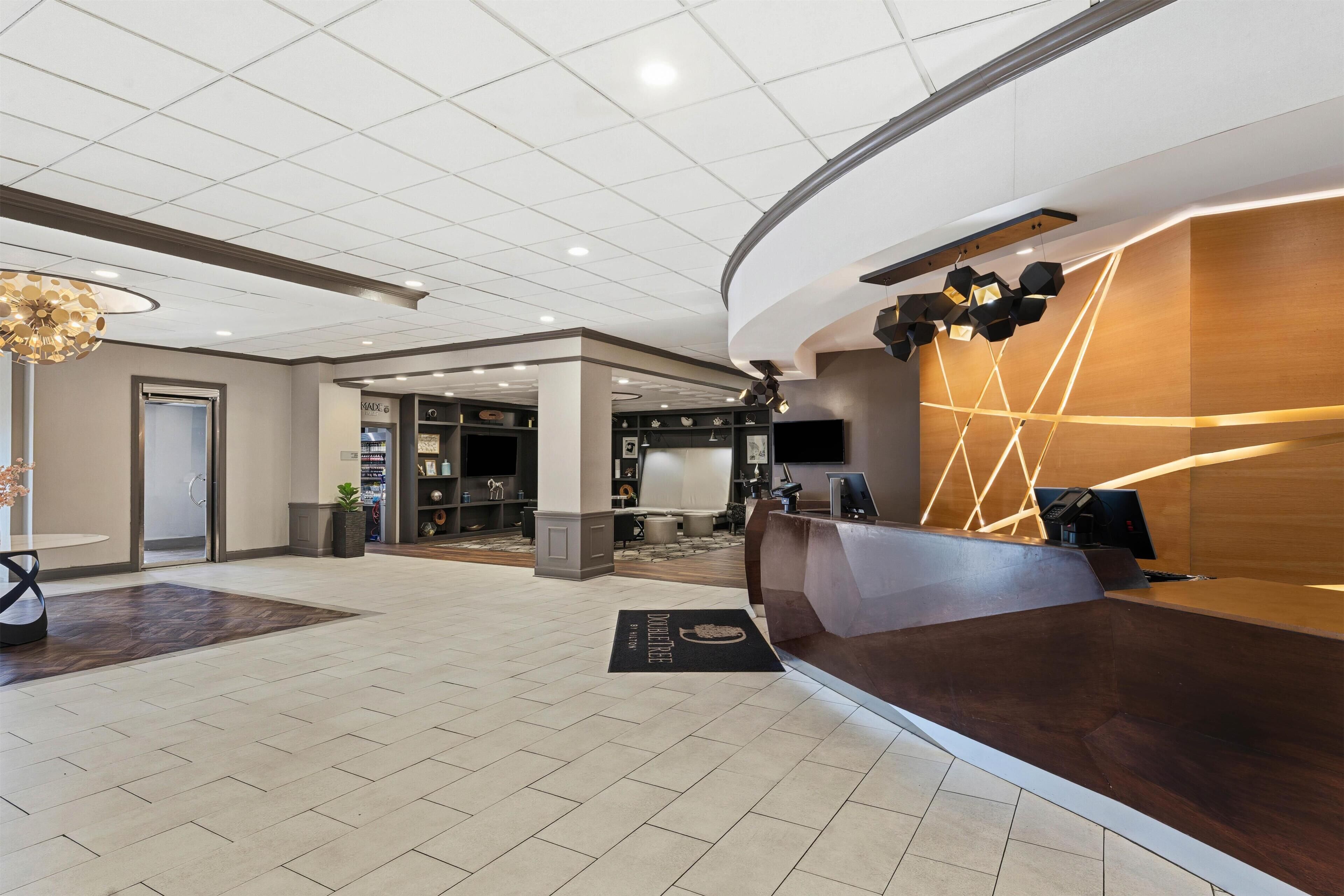 Zona de recepción de hotel con diseño moderno, que incluye un mostrador de recepción, un área de estar y un pasillo que da a otras habitaciones.