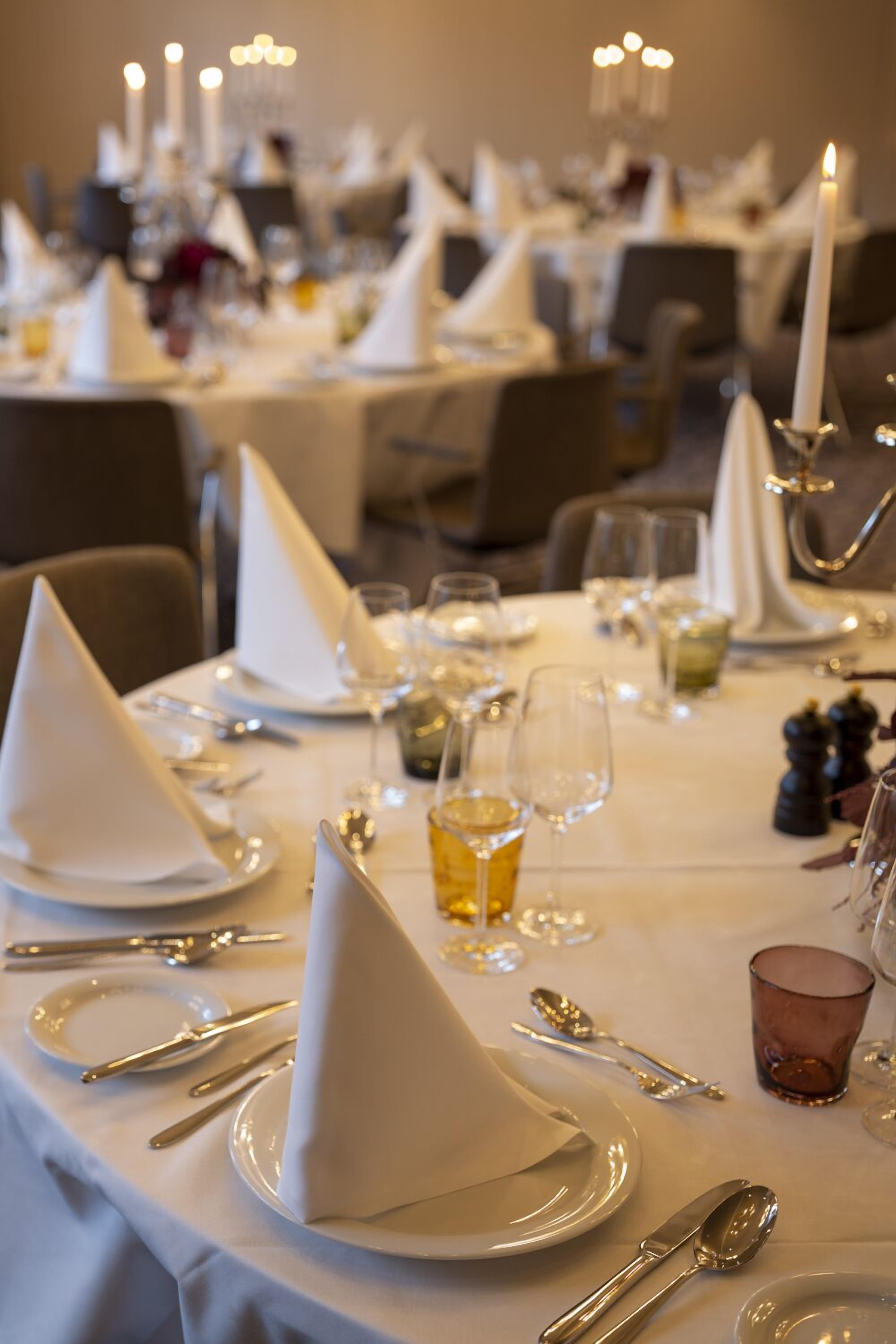 Comedor con mesas dispuestas para una comida, con manteles blancos, cubiertos y copas.