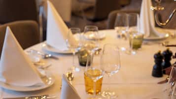 A dining area with tables set for a meal, featuring white tablecloths, silverware, and glasses.
