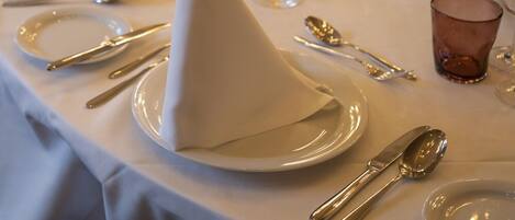 Comedor con mesas dispuestas para una comida, con manteles blancos, cubiertos y copas.