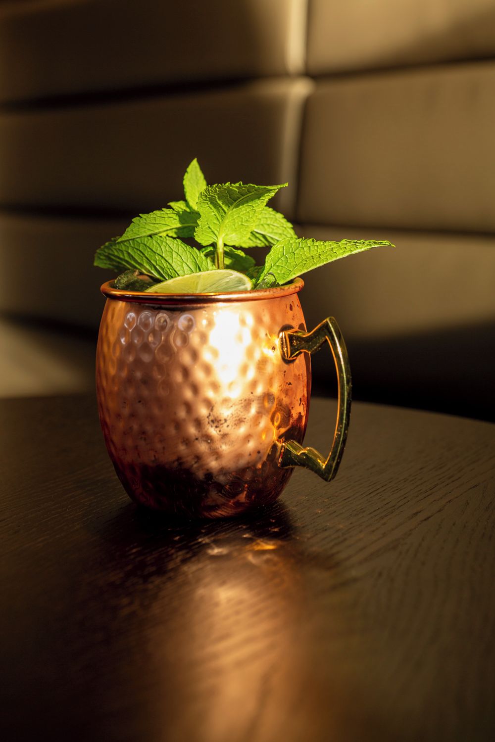 A copper mug with a handle, filled with a green liquid and mint leaves, placed on a wooden surface.