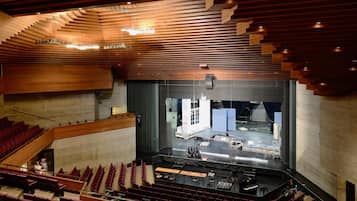 Un auditorio moderno con asientos escalonados, un escenario con instrumentos musicales y un amplio espacio abierto con vistas a la ciudad.
