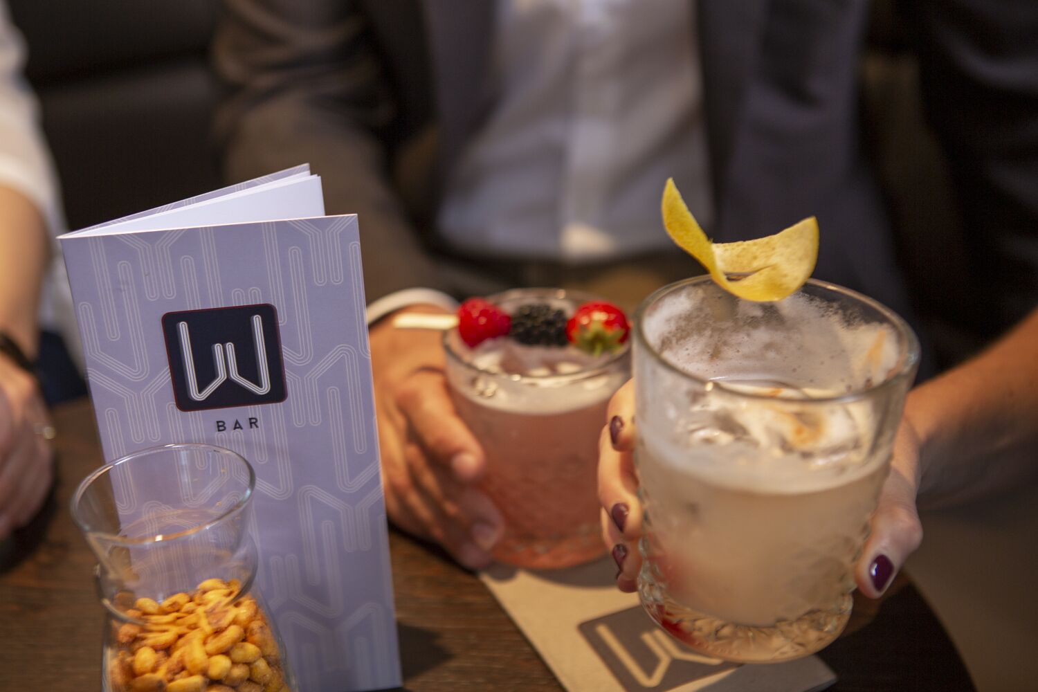 A menu with a logo, a glass of a beverage with a garnish, and a dessert with berries and a strawberry.