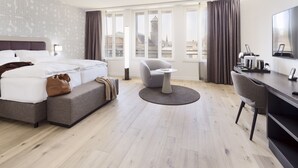 Habitación de hotel moderna con una cama grande, un escritorio, una silla y vistas a un paisaje urbano.