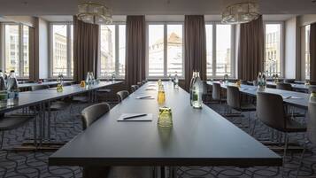 Une salle de conférence avec de longues tables, des chaises et des bouteilles d’eau.