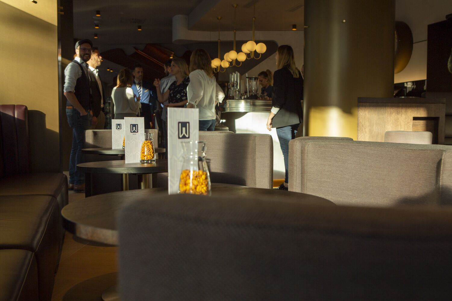 Interior de un restaurante con mesas redondas, asientos acolchados y una zona de bar.