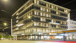 Un hotel de varios pisos con fachada de vidrio moderna, señalización iluminada y un bar visible.