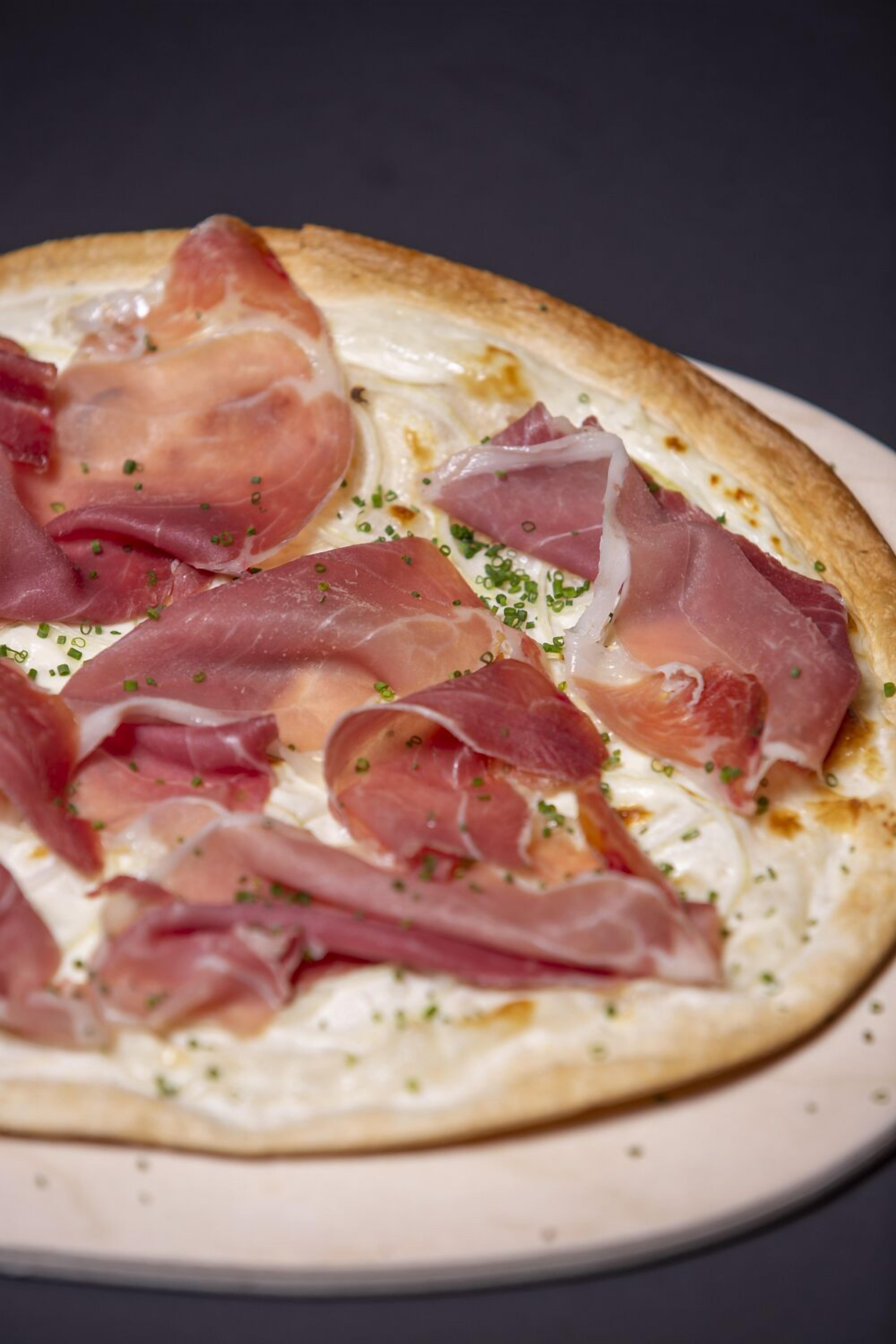 Pizza con prosciutto y cebollas verdes sobre un plato blanco.