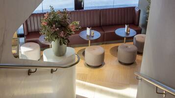 Een moderne zithoek met een bank en ronde tafels, een trap en uitzicht op zee.